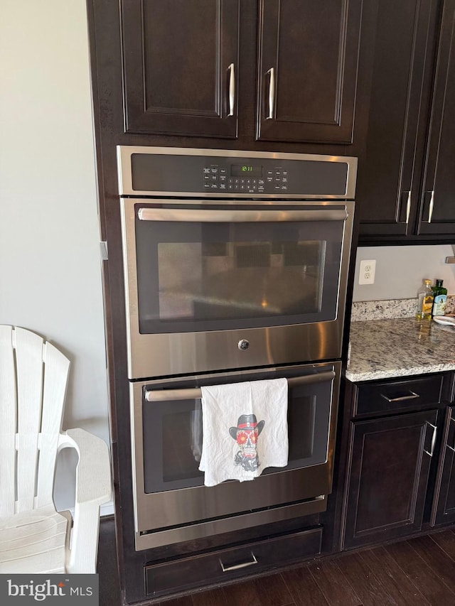 kitchen featuring dark brown cabinets, light stone countertops, dark wood-type flooring, and double oven