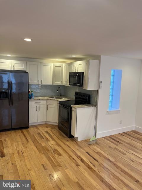 kitchen with white cabinets, light wood-type flooring, sink, and black appliances