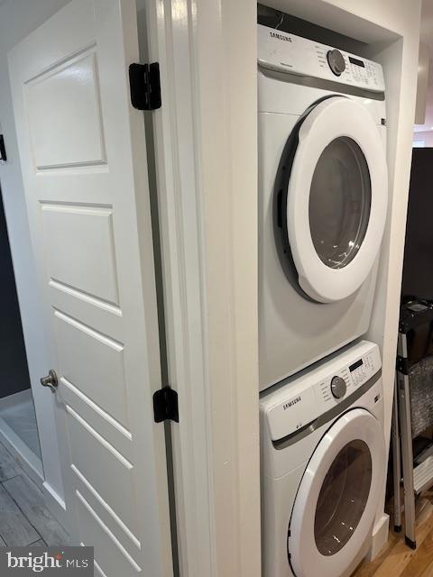 laundry room with hardwood / wood-style floors and stacked washer and dryer