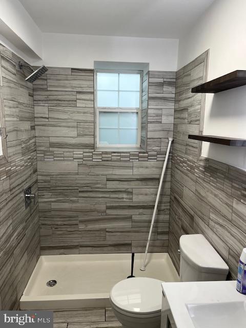 bathroom featuring vanity, toilet, tiled shower, and tile walls