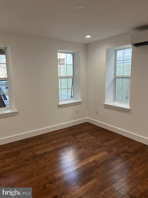 empty room with a wealth of natural light, dark hardwood / wood-style floors, and a wall mounted air conditioner