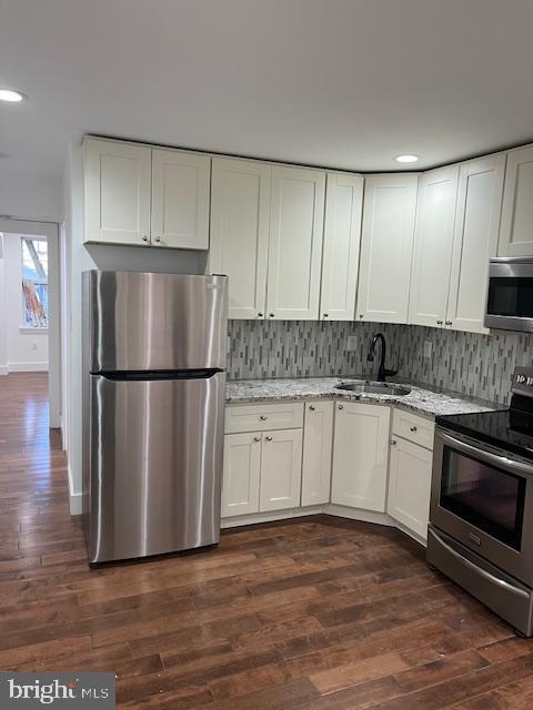 kitchen with white cabinets, appliances with stainless steel finishes, dark hardwood / wood-style floors, and sink