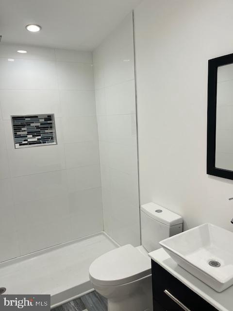 bathroom featuring tiled shower, hardwood / wood-style floors, vanity, and toilet