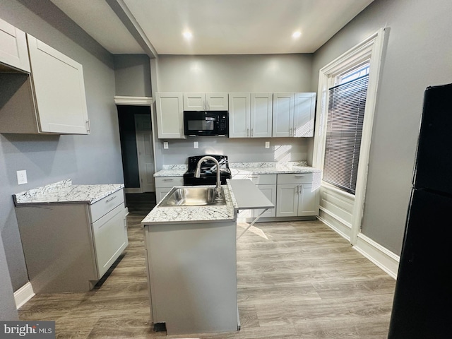 kitchen featuring a kitchen island with sink, sink, black appliances, and light hardwood / wood-style floors