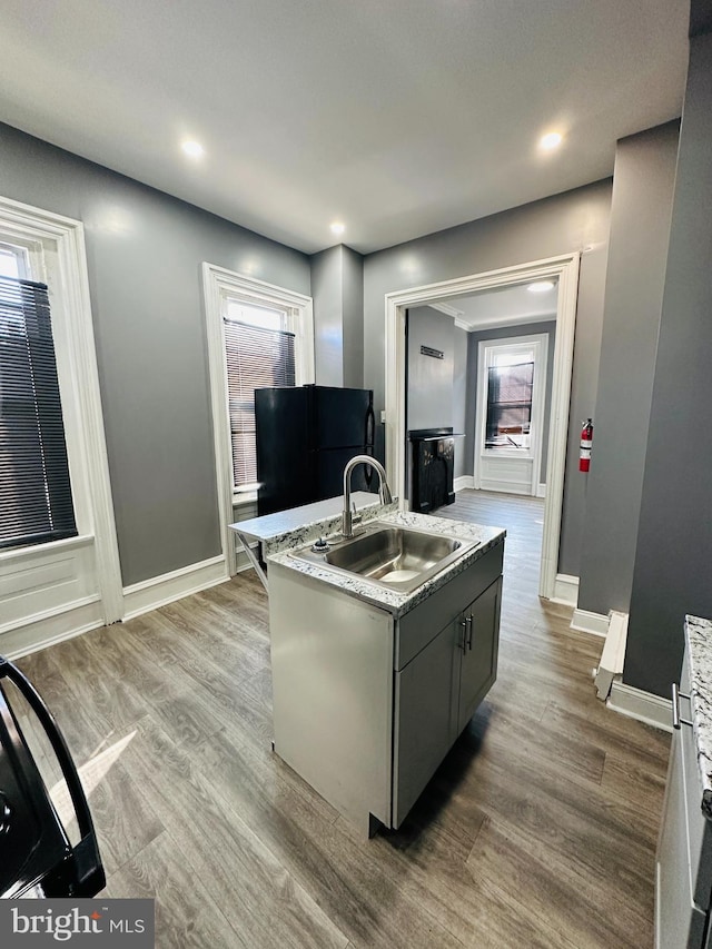 kitchen featuring gray cabinetry, light stone countertops, sink, light hardwood / wood-style flooring, and a center island with sink