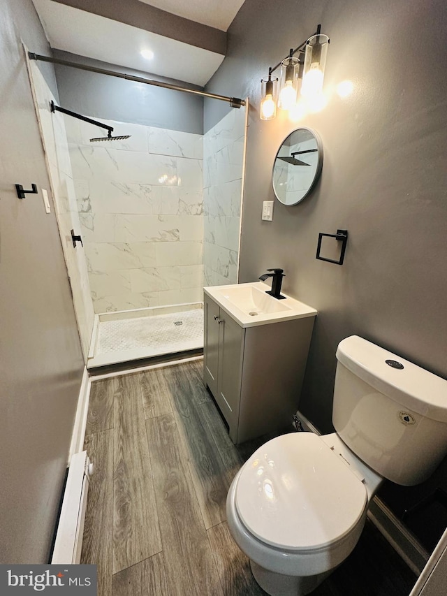 bathroom featuring vanity, a baseboard heating unit, tiled shower, hardwood / wood-style flooring, and toilet