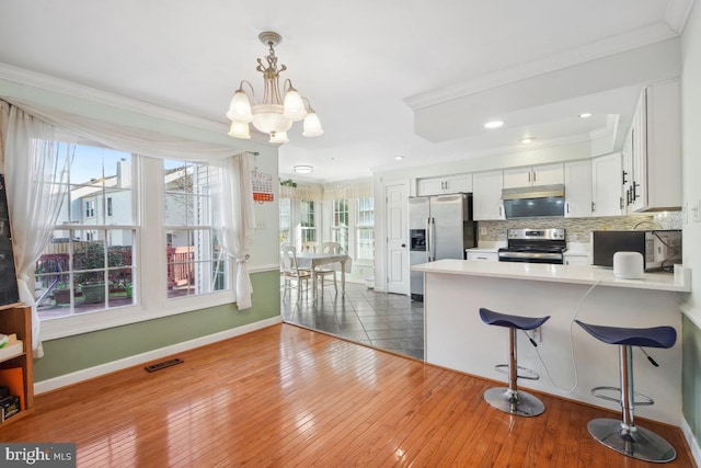 kitchen featuring appliances with stainless steel finishes, crown molding, dark wood-type flooring, a notable chandelier, and white cabinetry