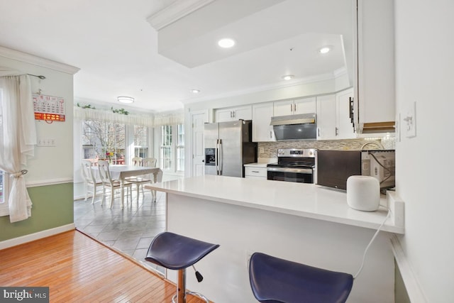 kitchen featuring white cabinetry, kitchen peninsula, light hardwood / wood-style floors, appliances with stainless steel finishes, and ornamental molding