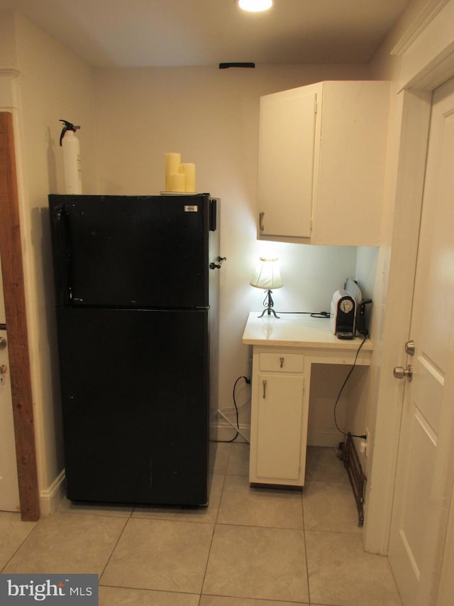 interior space with white cabinetry, black fridge, and light tile patterned flooring