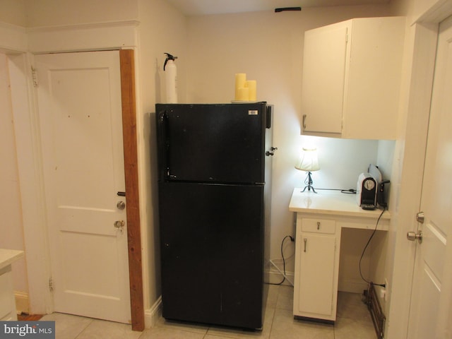 kitchen with black refrigerator, white cabinetry, and light tile patterned floors