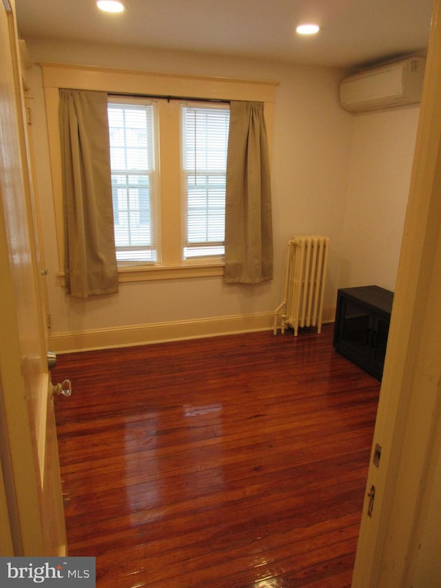 spare room featuring a wall mounted air conditioner, dark hardwood / wood-style flooring, and radiator