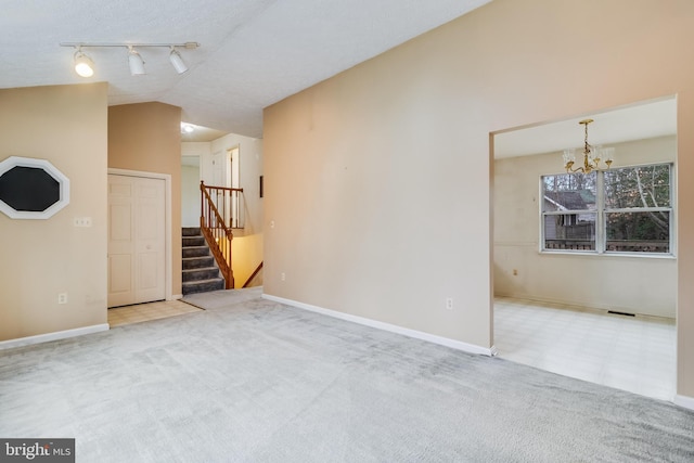 carpeted empty room with track lighting, lofted ceiling, and a notable chandelier