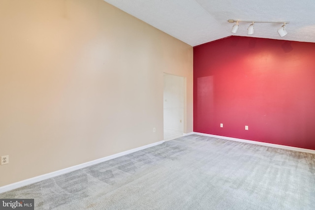 carpeted empty room with a textured ceiling, track lighting, and lofted ceiling