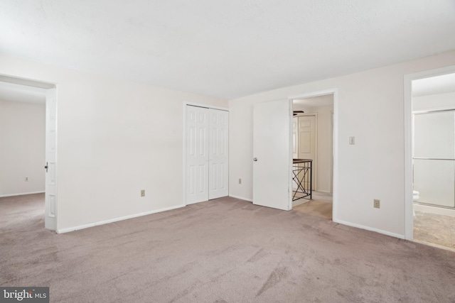 unfurnished bedroom featuring ensuite bathroom, a closet, and light colored carpet