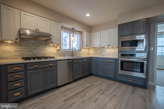 kitchen with appliances with stainless steel finishes, light wood-type flooring, tasteful backsplash, and sink