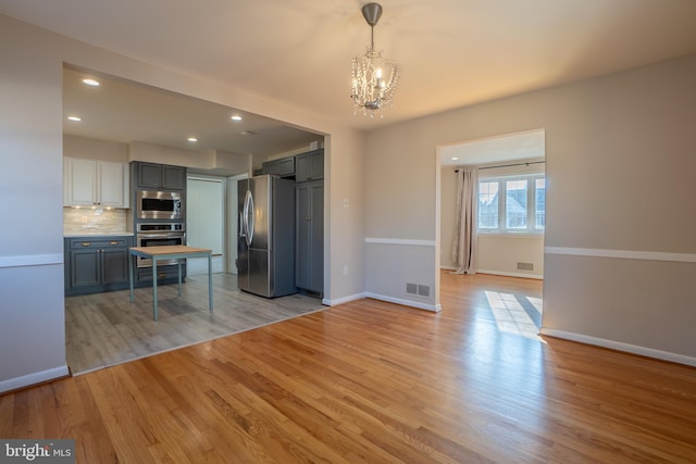 kitchen with light wood-type flooring, stainless steel appliances, tasteful backsplash, and gray cabinetry