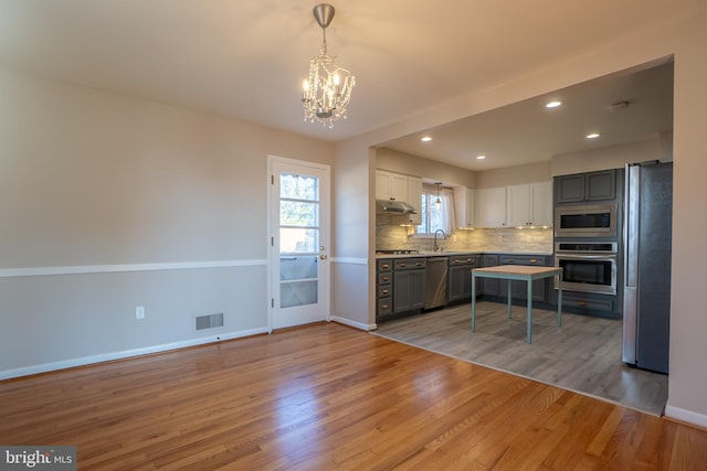 kitchen with appliances with stainless steel finishes, light wood-type flooring, white cabinetry, and hanging light fixtures