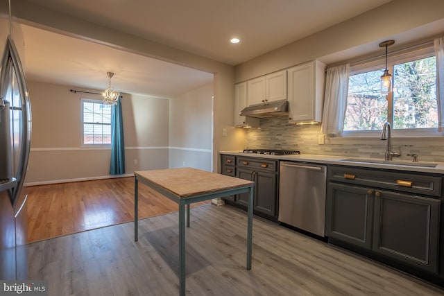 kitchen featuring appliances with stainless steel finishes, light wood-type flooring, sink, pendant lighting, and white cabinets