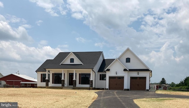 modern farmhouse with aphalt driveway, board and batten siding, an attached garage, and fence