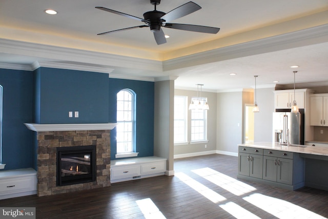 unfurnished living room with baseboards, dark wood-style flooring, ceiling fan, a stone fireplace, and crown molding