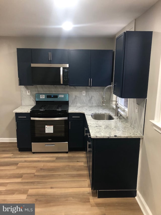 kitchen featuring stainless steel appliances, light stone counters, light hardwood / wood-style floors, and sink