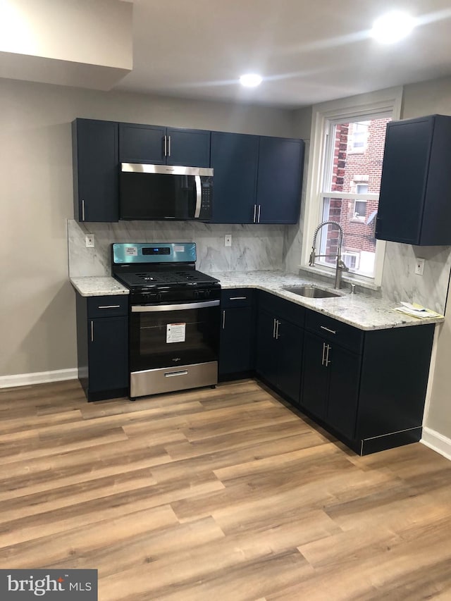 kitchen with light stone countertops, sink, backsplash, light hardwood / wood-style floors, and appliances with stainless steel finishes