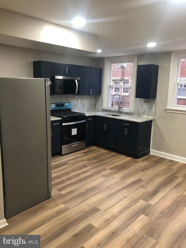 kitchen with appliances with stainless steel finishes, light wood-type flooring, backsplash, and sink