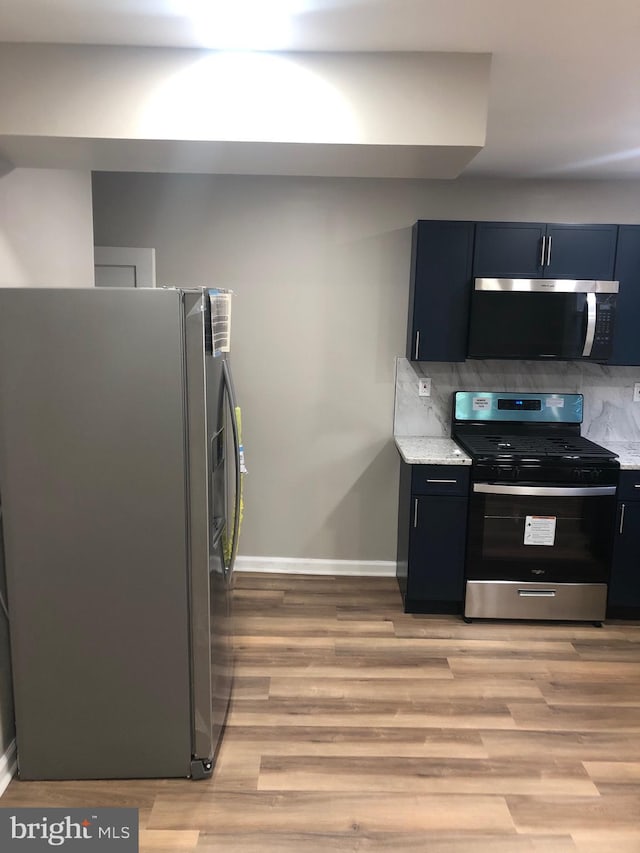 kitchen featuring decorative backsplash, light stone countertops, appliances with stainless steel finishes, and light hardwood / wood-style flooring