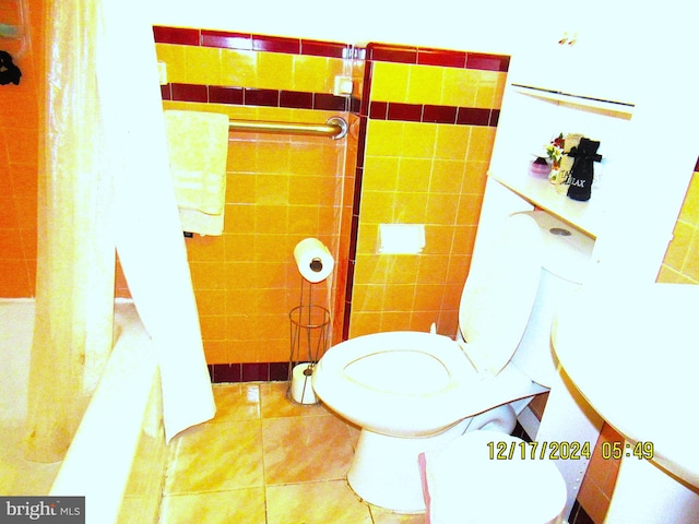 bathroom featuring tile patterned floors, toilet, tile walls, and shower / bath combo with shower curtain