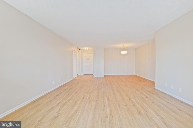 empty room featuring a chandelier, light wood-type flooring, and baseboards