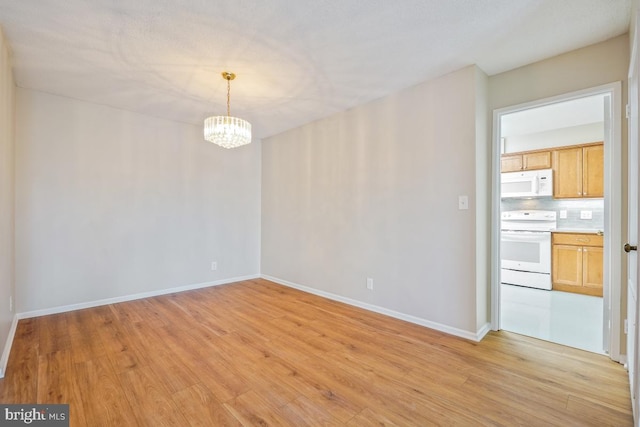 unfurnished room featuring light wood-style floors, baseboards, and a notable chandelier