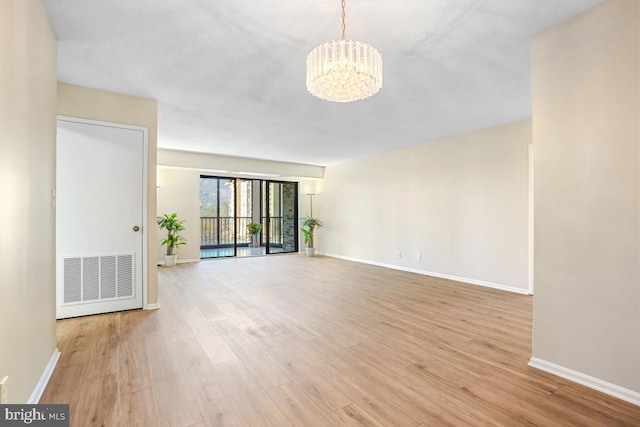 unfurnished living room featuring light wood finished floors, baseboards, visible vents, and a notable chandelier