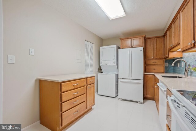 kitchen featuring white appliances, brown cabinetry, a sink, and stacked washer and clothes dryer