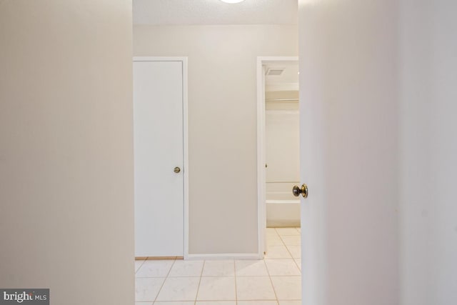 hallway featuring light tile patterned flooring, a textured ceiling, and baseboards