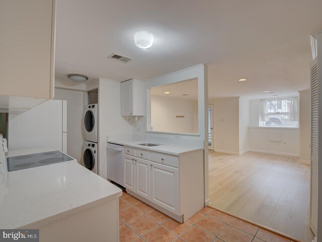 kitchen with stove, white cabinets, stainless steel dishwasher, light hardwood / wood-style floors, and stacked washer / dryer