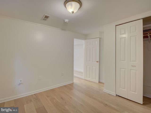 unfurnished bedroom featuring a closet, ornamental molding, and light wood-type flooring