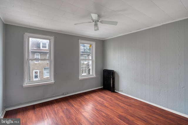 empty room with radiator, crown molding, a wealth of natural light, and dark wood-type flooring