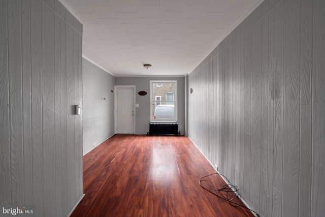 hall with radiator heating unit, hardwood / wood-style flooring, and wood walls