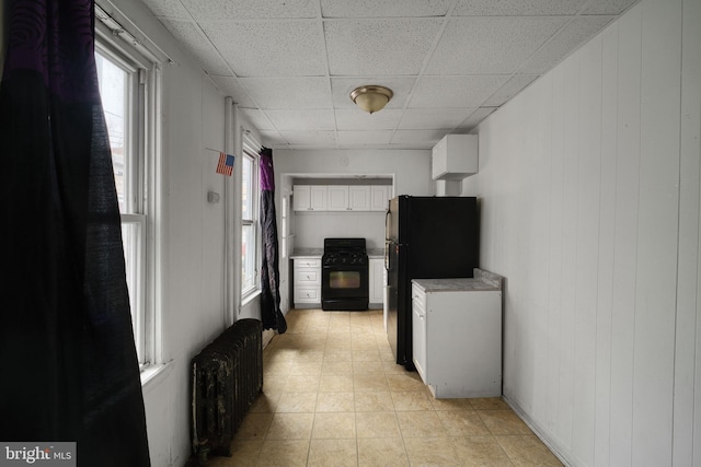 corridor with wooden walls, radiator heating unit, light tile patterned floors, and a drop ceiling