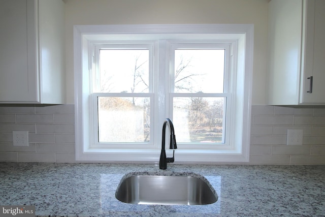 interior space with light stone countertops, tasteful backsplash, white cabinetry, and sink