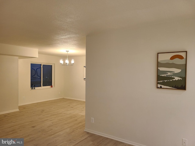 unfurnished room with hardwood / wood-style floors, a textured ceiling, and a notable chandelier