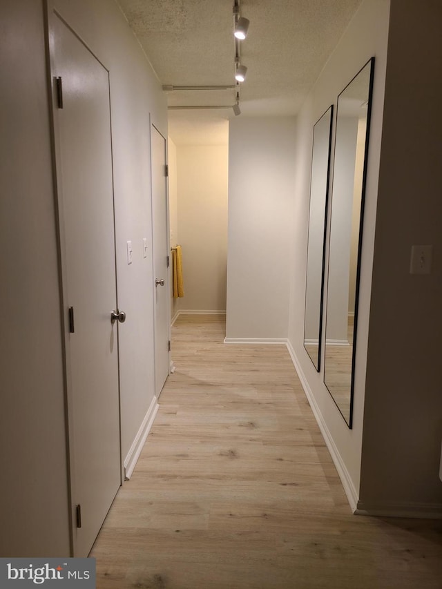 corridor with light hardwood / wood-style flooring, rail lighting, and a textured ceiling