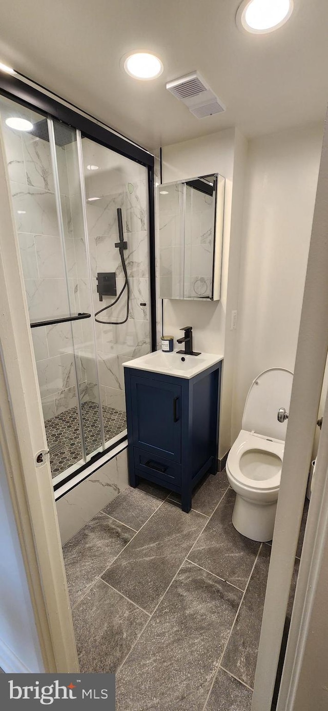 bathroom featuring vanity, a shower with shower door, and toilet