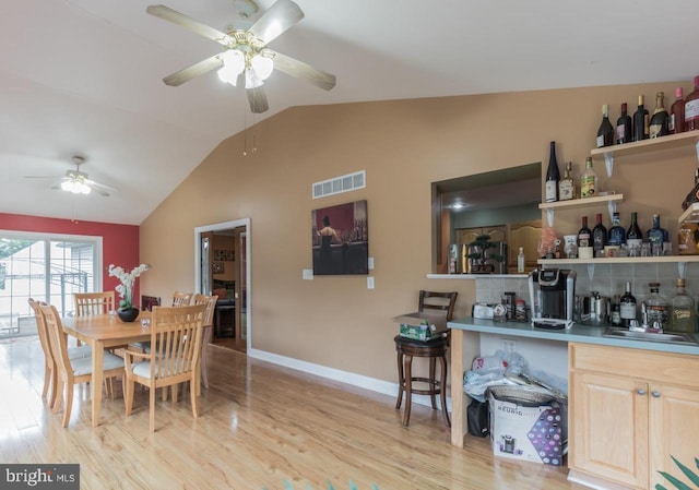 dining space featuring ceiling fan, light hardwood / wood-style flooring, lofted ceiling, and wet bar