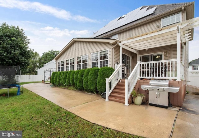 back of property with solar panels, an outbuilding, and a trampoline