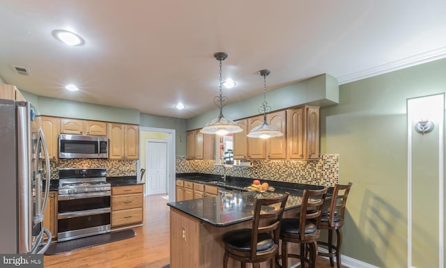 kitchen with a kitchen breakfast bar, backsplash, light hardwood / wood-style floors, pendant lighting, and appliances with stainless steel finishes