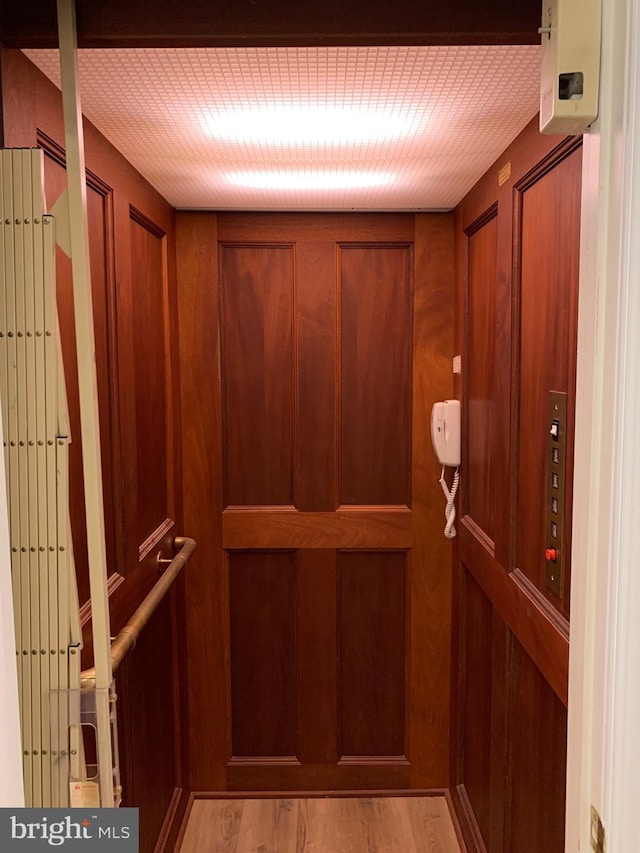 interior details with elevator, wood walls, and hardwood / wood-style floors