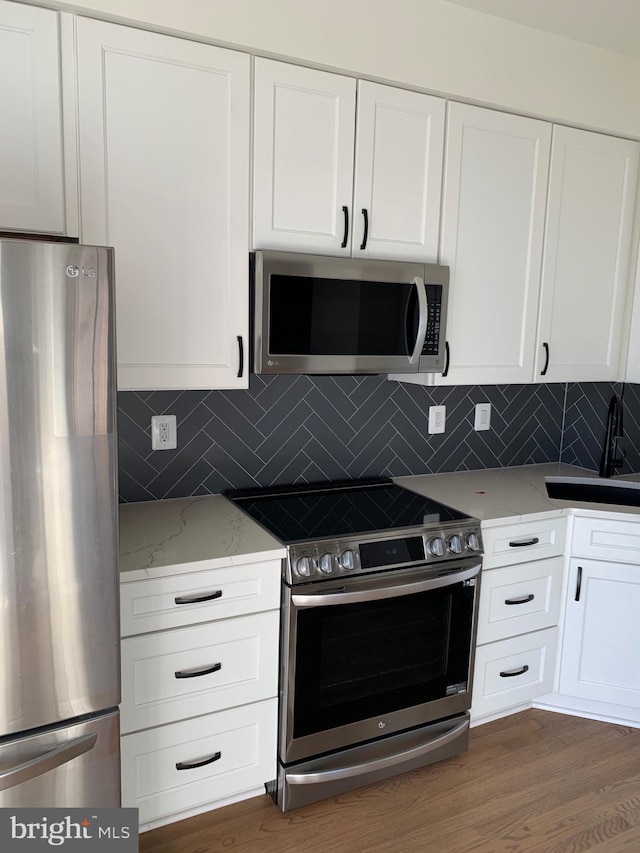 kitchen with dark hardwood / wood-style floors, light stone countertops, white cabinetry, and stainless steel appliances