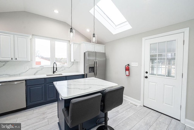 kitchen with sink, vaulted ceiling with skylight, a kitchen island, white cabinetry, and stainless steel appliances