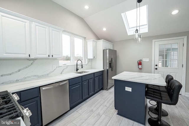 kitchen featuring hanging light fixtures, sink, vaulted ceiling with skylight, appliances with stainless steel finishes, and white cabinetry